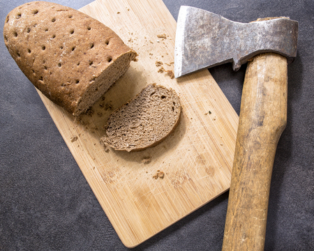 hard stale bread and cut off a piece of it lie on a wooden cutting board, axe lying besideの写真素材