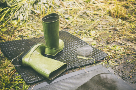 Children green boots left in the rainy weather outdoor one is filled with by rainwater, on a background green grassの写真素材