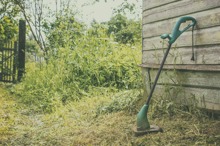 electric grass trimmer stands in the garden near the house, simply supported on the wallの写真素材