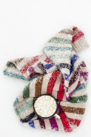Old metal cup of hot cocoa with marshmallows and a soft colorful knitted scarf on a fluffy the snowの写真素材