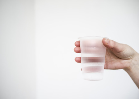 man holds in his hand a plastic matt a glass of pure drinking water on white backgroundの写真素材