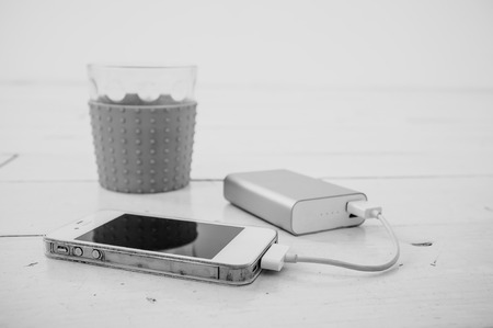 Smartphone being charged from a portable charging device, nearby there is a incomplete glass of tea with lemonの写真素材