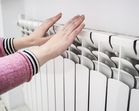 Girl warms the frozen hands above a hot of the radiator, close upの写真素材