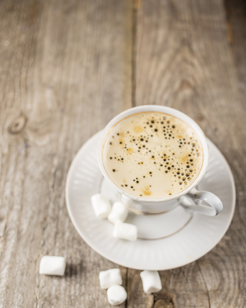 Hot black coffee in a cup with marshmallows on the old a wooden tableの写真素材
