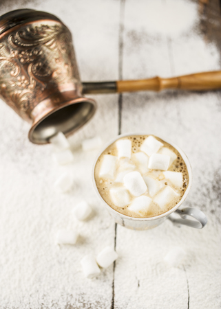 Hot black coffee in a cup with marshmallows cuzve nearby there is on the old a wooden table sprinkle with powdered sugarの写真素材