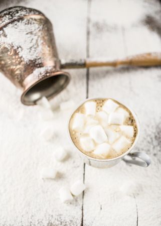 Hot black coffee in a cup with marshmallows cuzve nearby there is on the old a wooden table sprinkle with powdered sugarの写真素材