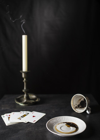 Fortune teller reading coffee grounds in the state are near a deck of cards and a candle in the old candlestick against the black backgroundの写真素材
