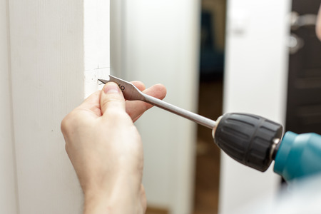 Man drilling a hole in a wooden the door in a roomの写真素材