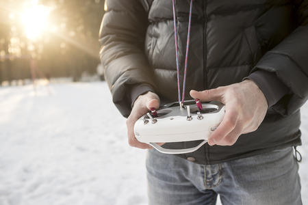 man holding a remote control of drone, standing in a snowy winter park outdoors
