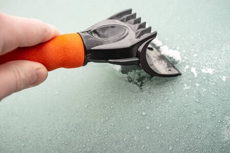 Mans hand cleans hoarfrost from a window glass in a car with a scraper, on a frosty morning.の写真素材