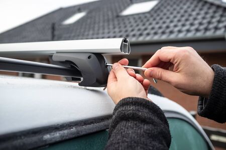 Man with a screwdriver installs attachments for trunk or cargo box on roof of the car.の写真素材