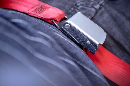 Man is fastened with a seat belt, red with a metal buckle, in an airplane. Safe flight concept.の写真素材