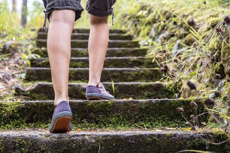 Womens legs in comfortable sneakers, going up the old stone steps. Concept of an active lifestyle.