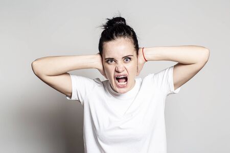 Woman is furious. She covered her ears with hands, opened mouth and screams loudly, looking with...