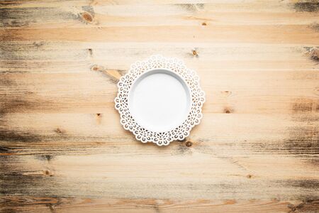 Empty, round white plate, with a beautiful carved floral pattern on the rim. Textured wood background.の写真素材