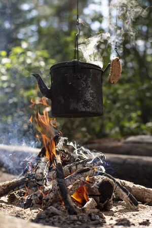 Boiling, zakopchonny maker with a hot drink and a piece of bread as toast, hanging on hooks over the campfire in a forest.の写真素材