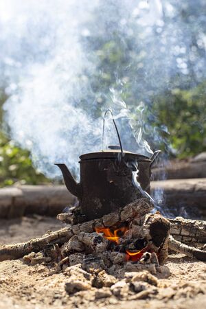 Boiling, sooty kettle with hot drink stands on a campfire in the smoke, in a forest.の写真素材