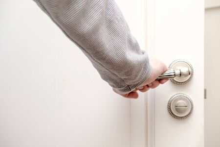 Human hand holding on to a beautiful carved, metal handle in an open wooden door, painted in white color.の写真素材