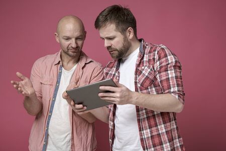 Two puzzled men, with a serious expression on their faces, are discussing some problem, looking at the tablet.の写真素材