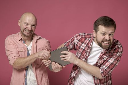 Two men hungrily snatch each other tablet from a friend and gritted his teeth, during the sale.の写真素材