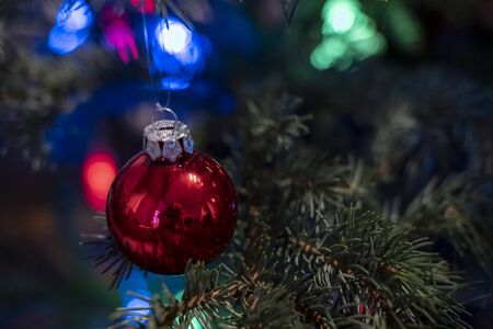 Bright, red glass toy ball on a Christmas tree, on a blurred background of garland.の写真素材
