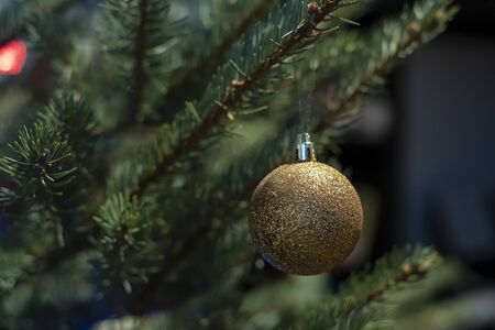 Bright, brilliant gold-colored glass toy ball on a Christmas tree, on a blurred background of garland.の写真素材