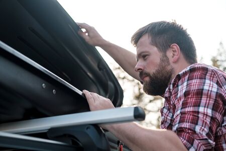 Focused bearded man peers into an open roof rack on a car or in a cargo box. Preparing to leave.の写真素材