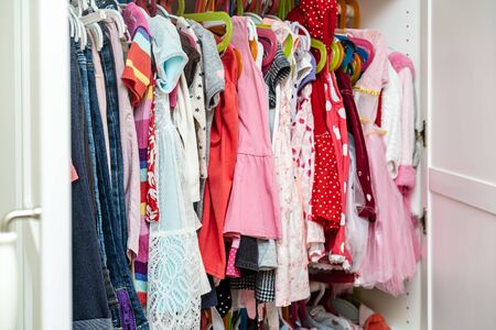 Large selection of bright, colored children's clothes for a girl hanging in a closet, on hangers.の写真素材