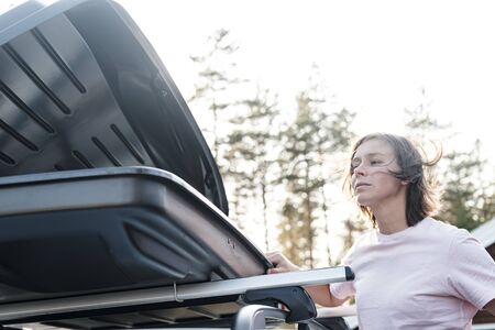 Open trunk or cargo box, which is located on the roof of a car and a woman peeking into it. Preparing for a vacation.の写真素材