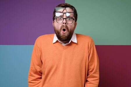 Strange, shocked bearded man put on three pairs of glasses, opened mouth in surprise and with big...