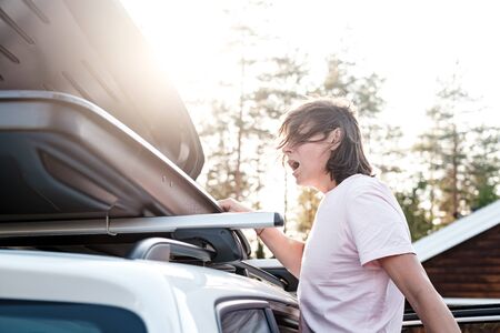 Woman looks into the open trunk or cargo box, which is located on the roof of the car and realizes that she forgot something important and opens mouth in confusion. Family vacation..の写真素材