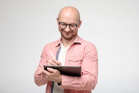 Joyful, cute smiling man in glasses, works with a tablet and stylus pen.の写真素材
