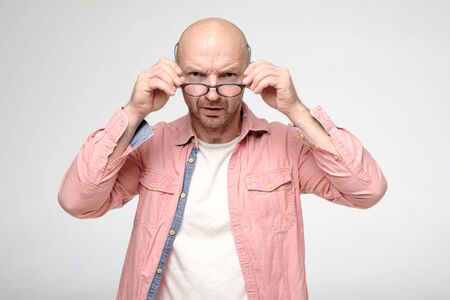 Angry, frowned man strictly looks into the camera over the glasses that he holds with hands.の写真素材