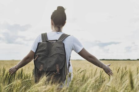 Woman stands on a wheat field triticum, touches the ear with hands and looks thoughtfully into the distance. Freedom concept.の写真素材