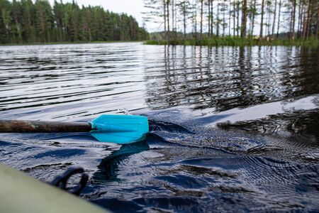 .Rowing an old oar with a wooden handle and a plastic blade, against the backdrop of a lake and forest, on a summer evening. View from an inflatable boat..の写真素材