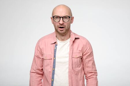 Shocked, upset bald man with glasses in a stupor, emotionally opened mouth and stares at the camera in disbelief.の写真素材