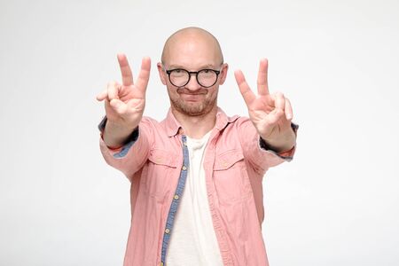 Satisfied, smiling man makes a V-sign with fingers, on two hands, looks at the camera with a funny expression on face.の写真素材