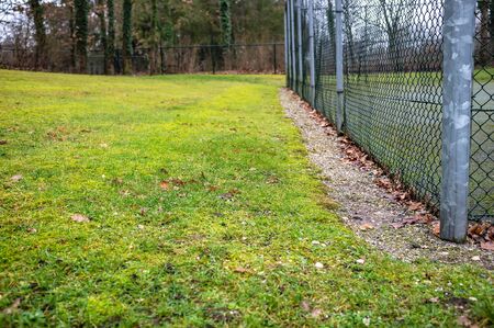 Angle playground surrounded by a welded wire fence and a lawn with a green grass, in a dull, cloudy spring day.の写真素材