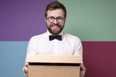 Funny man in round glasses holds a box with a gift in hands, he smiles and looks joyfully at the camera.の写真素材