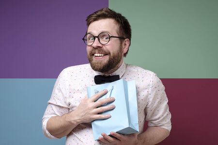 Man received a pleasant surprise, he is happy, joyfully presses a package with a gift to chest, smiles and looks at the camera.の写真素材