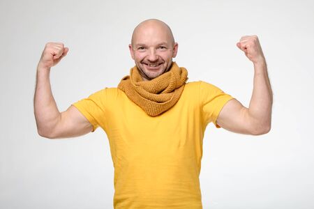 Strong, positive man in a bright yellow t-shirt and scarf, bent his arms and shows his muscles, smiles and looks at the camera.の写真素材