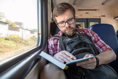 Focused bearded man riding in a train, reading a book and making notes with a pencil.の写真素材