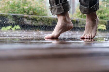 Barefoot female legs walk on the wooden floor of the courtyard, in the pouring summer rain, on a blurred background. Close-up.の写真素材
