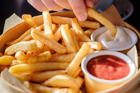 Appetizing French fries with sauce in a wooden dish, in natural light from the window. Close-up.の写真素材