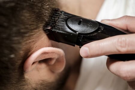 Female hand does cut hair on a mans head with a trimmer. Getting groomed. Close-up.の写真素材