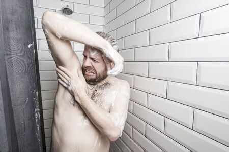 Man experiences discomfort due to irritation of the armpit after shaving, he stands soaped, in the shower, under a stream of waterの写真素材