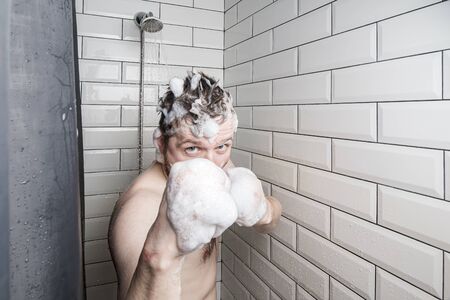 Athlete, for the sake of a joke, made boxing gloves from soap foam on fists, standing in the shower, under the stream of water.の写真素材