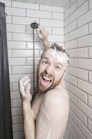 Positive man in soapy foam is having fun, because hot water has run out in his soul, he laughs and looks at the camera.の写真素材