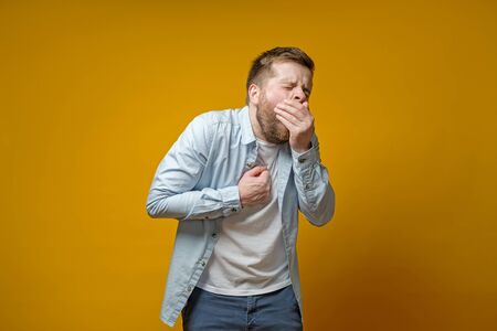 Man coughs, covering mouth with palm and holds hand on chest, experiencing pain. Concept of the spread of the virus.の写真素材