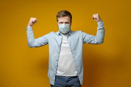 Satisfied man put on a medical mask on face and feels protected from viruses, showing a gesture of confidence with hands.の写真素材